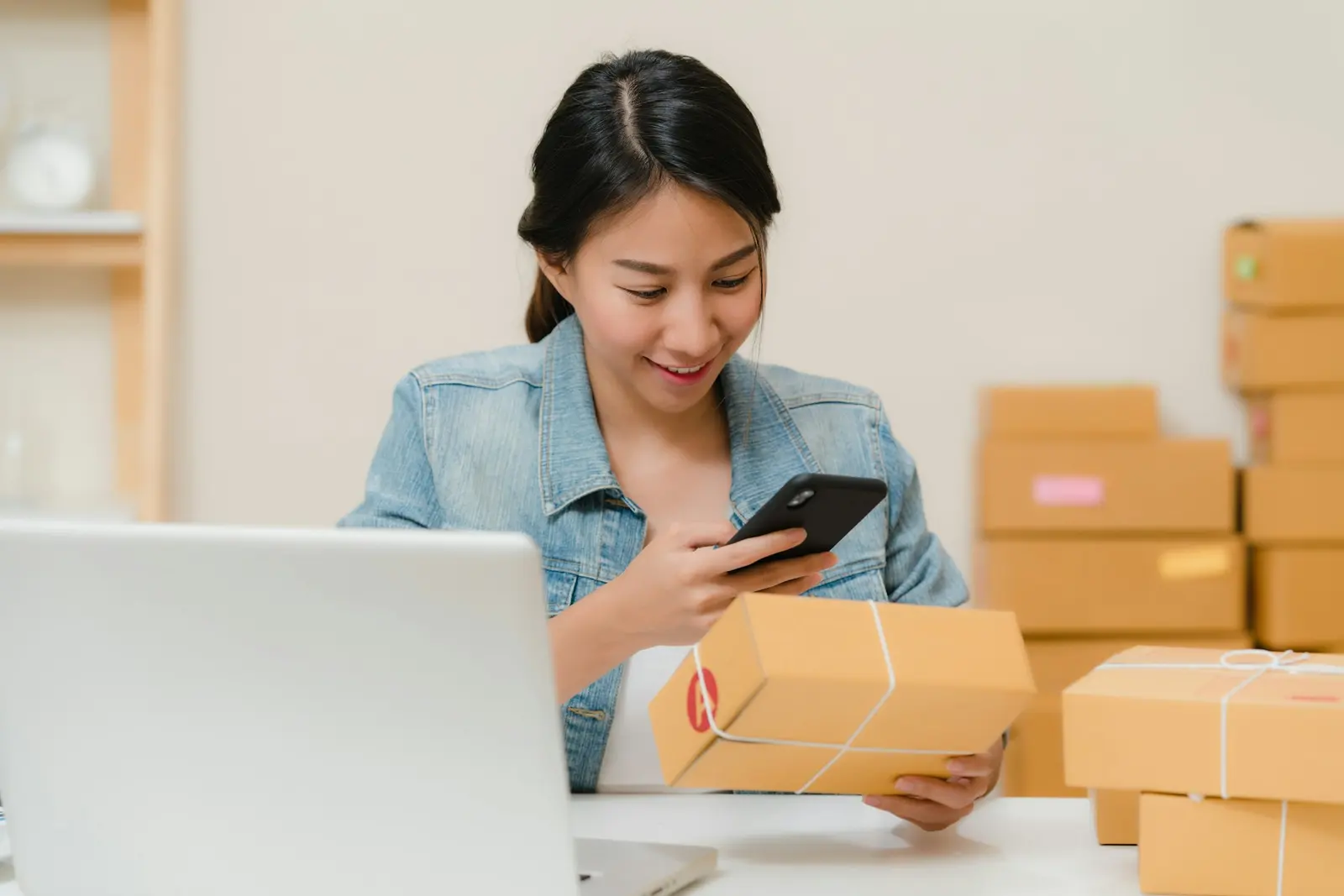 Online store owner checking an order on her phone next to packed shipping boxes